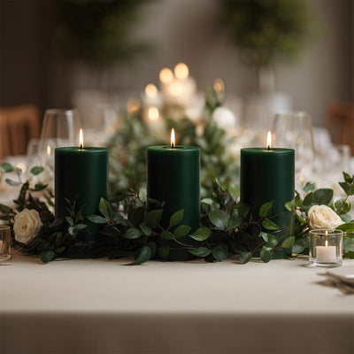 Green candles surrounded by greenery and roses on an elegant table setting.