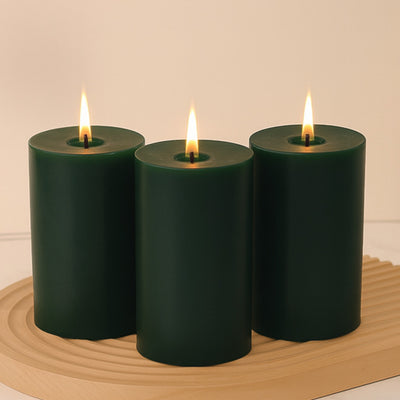 Green pillar candles with flames on a wooden tray.