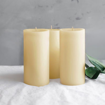 Three ivory pillar candles with a leaf on a soft gray background.
