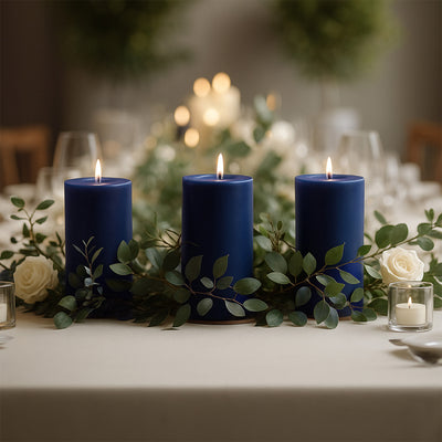 Three blue candles surrounded by greenery and white roses on a dining table.