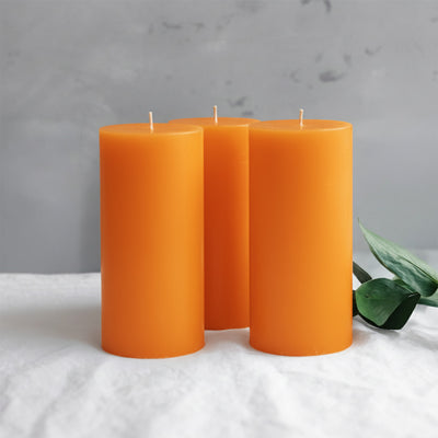 Three vibrant orange candles with green leaves on a light surface.