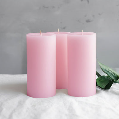 Pink frosted candles with greenery on a soft surface.