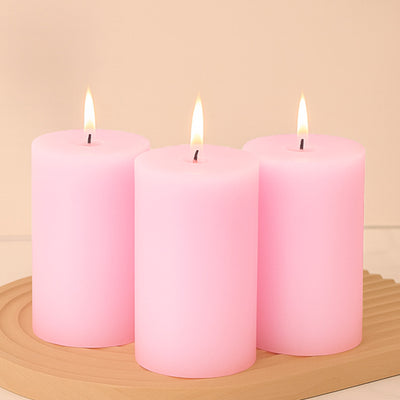 Three pink pillar candles with flames on a wooden tray.