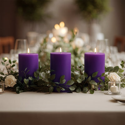 Three purple candles surrounded by greenery and white roses on a dining table.