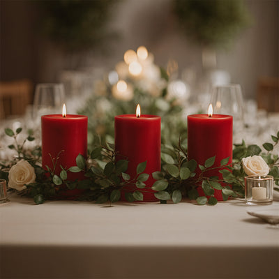 Red candles adorned with greenery and roses on an elegant dining table.