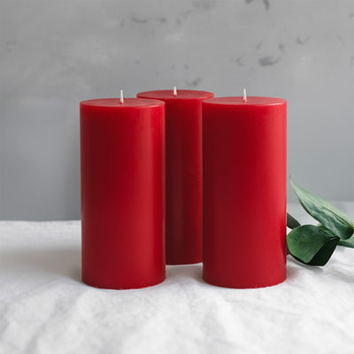 Three red candles with greenery on a textured surface.