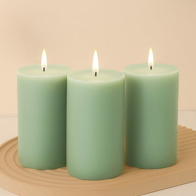 Three green pillar candles with flames on a wooden tray.