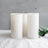 Set of three white candles with green leaves on a light background.