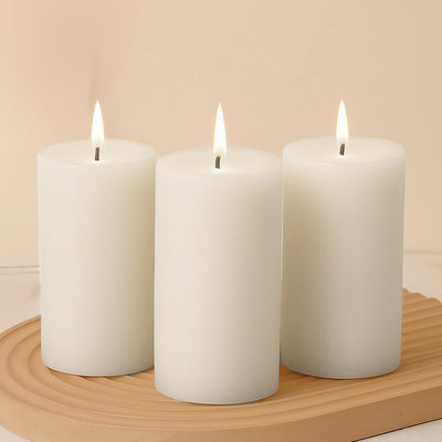 Three white pillar candles with flames on a wooden tray.