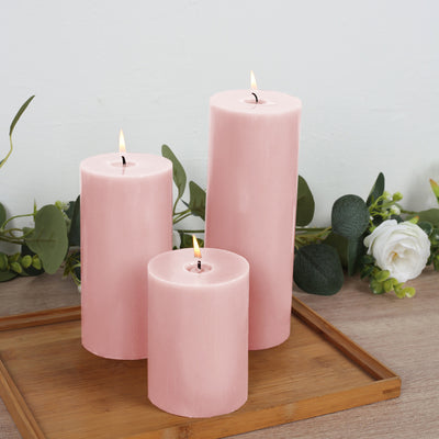 Pink candles in varying heights on a wooden tray with greenery backdrop.