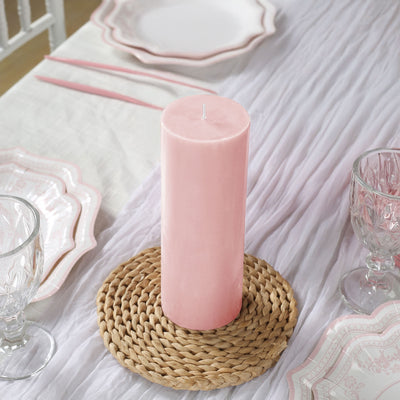 Pink pillar candle on woven placemat, surrounded by elegant table setting.