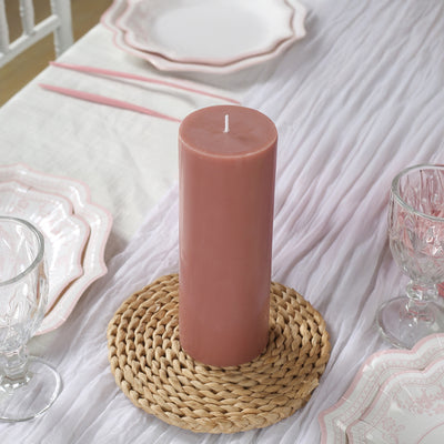 Pink pillar candle on a woven placemat with elegant table setting.