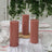 Three pink pillar candles on a table with glassware and greenery.