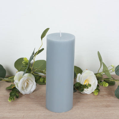 Gray pillar candle surrounded by greenery and flowers.