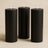 Set of three tall black candles on a neutral background.