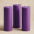 Purple pillar candles in varying heights against a soft beige backdrop.