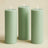 Green pillar candles in varying heights on a beige background.