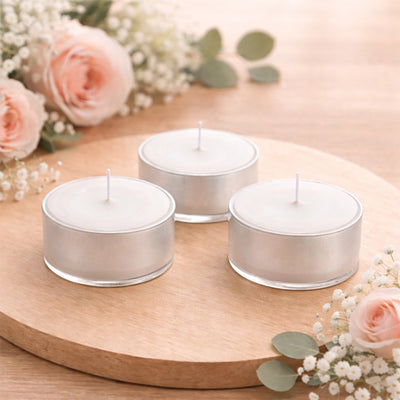 Three silver tealight candles on a wooden surface with roses and greenery.