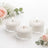 Three white candles in glass holders surrounded by flowers.