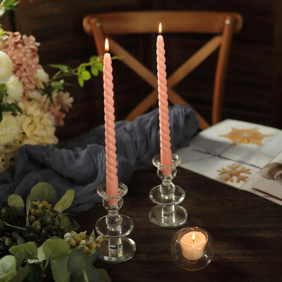 Pink spiral candles in glass holders on a rustic table with flowers and a candle.