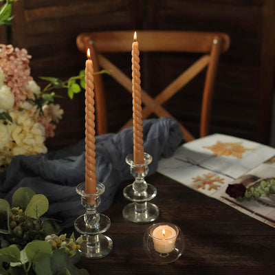 Two twisted candles in glass holders with a lit tealight, surrounded by flowers and decor.