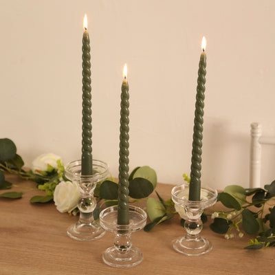 Green twisted candles in glass holders with greenery accents.