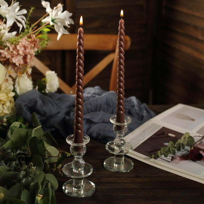 Twisted brown candles in clear holders, surrounded by floral decor and fabric.