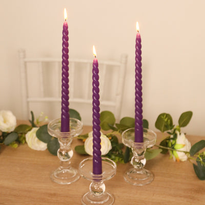 Purple twisted candles in glass holders with greenery decor.