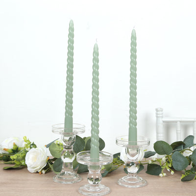 Twisted green candles in glass holders with greenery accents.