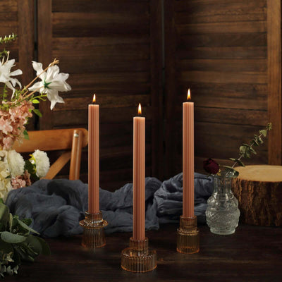 Three pink taper candles in glass holders, lit on a rustic wooden table.