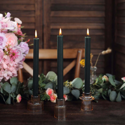 Elegant black taper candles in stylish holders, surrounded by flowers and greenery.