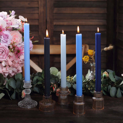 Colorful tapered candles in glass holders on a rustic table with flowers.
