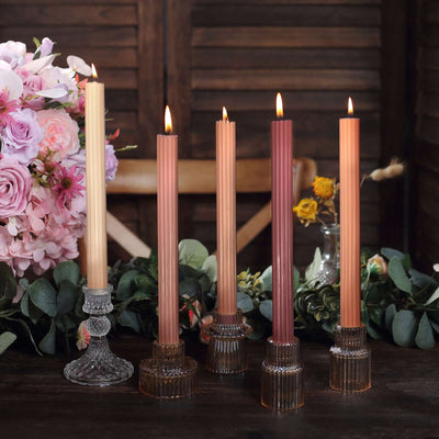 Elegant taper candles in various shades with decorative holders on a rustic table.