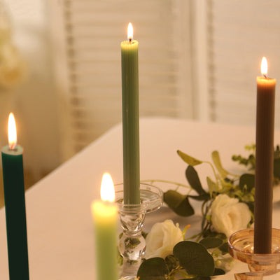 Colorful candles in elegant holders surrounded by greenery and flowers.
