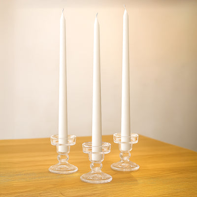 Three tall white candles in clear glass holders on a wooden table.