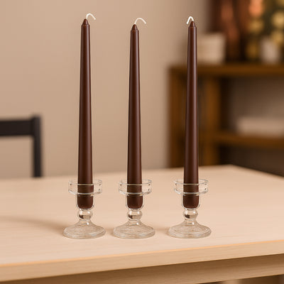 Brown taper candles in glass holders on a wooden table.