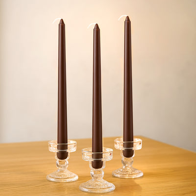 Three brown taper candles in crystal holders on a wooden table.