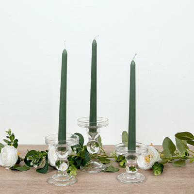 Green tapered candles in clear glass holders with white roses and greenery.