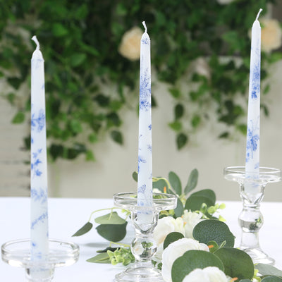 Blue floral candles in crystal holders on a table with greenery.