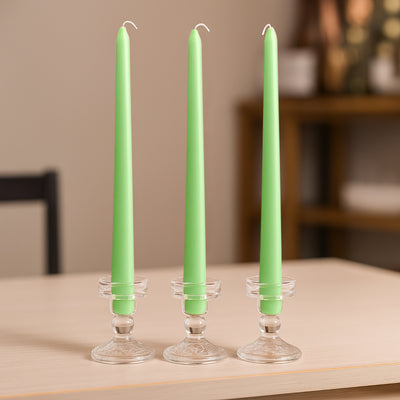 Three green candles in clear holders on a wooden table.