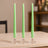Three green candles in clear holders on a wooden table.