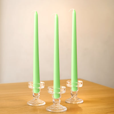 Three green taper candles in clear glass holders on a wooden table.