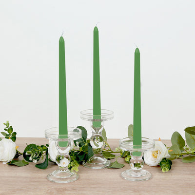 Green taper candles in clear holders with greenery and white flowers.