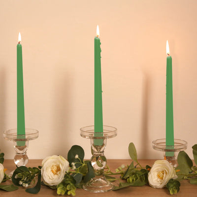 Green taper candles in crystal holders with white flowers and greenery.