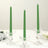 Green tapered candles in clear glass holders on a table.