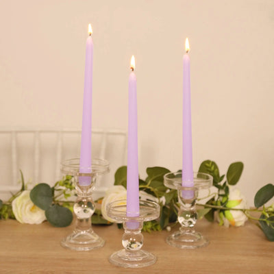 Purple taper candles in elegant glass holders with greenery and flowers.