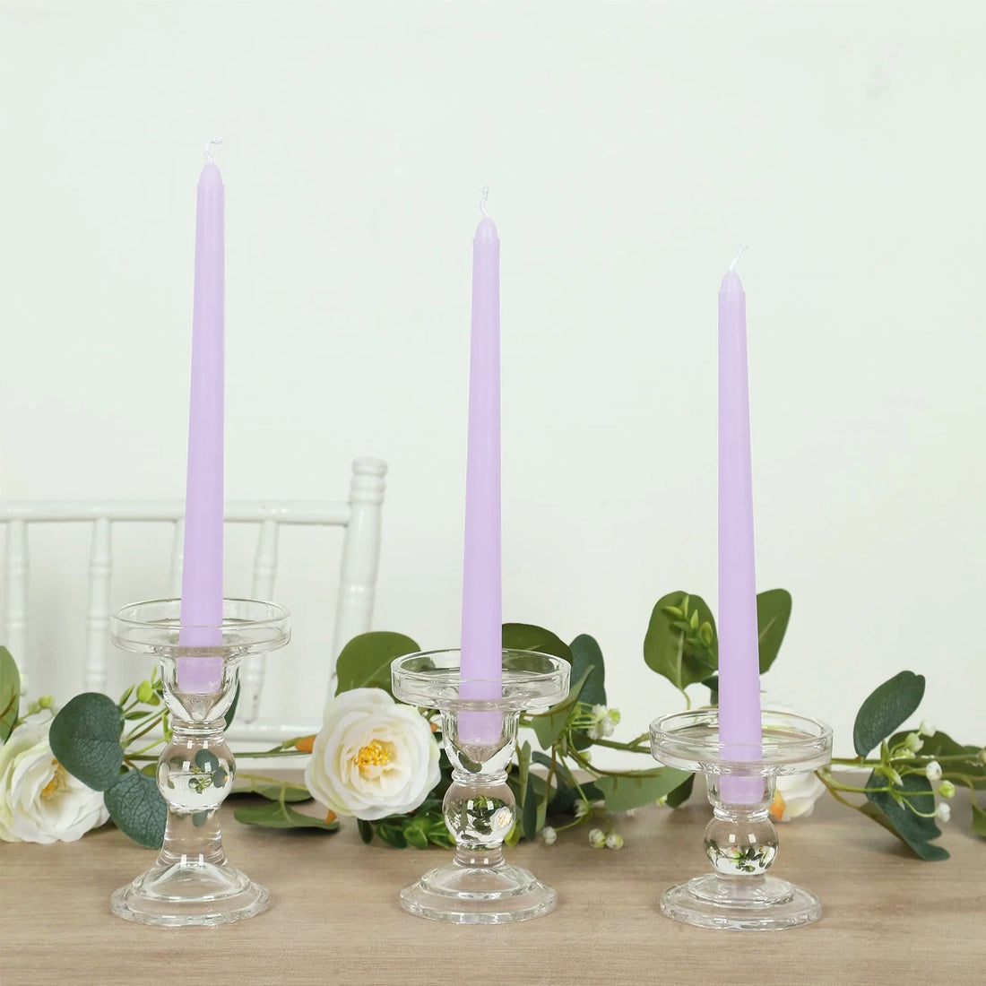 Purple taper candles in clear glass holders with greenery accents.