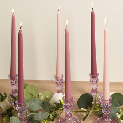 Elegant tapered candles in various shades on decorative candle holders with greenery.