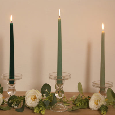 Colorful taper candles in glass holders with greenery and flowers.