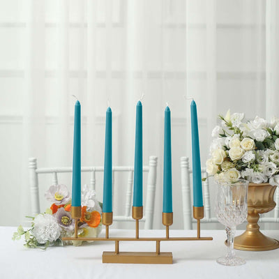 Teal tapered candles in a gold holder with flowers and glassware